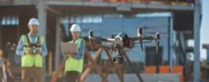 Two construction workers operate a survey drone on a work site.
