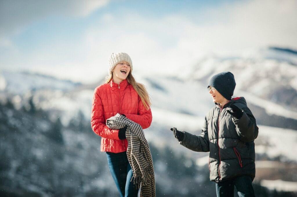 A brother and sister together outdoors in the winter, laughing.