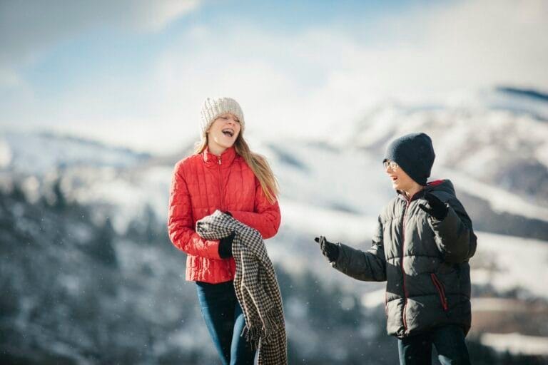 A brother and sister together outdoors in the winter, laughing.