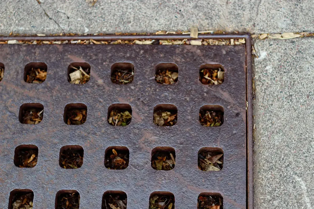 What Engineering Services Are Needed for a Residential Land Development Project? 3 a stormwater catch basin or drain grate with holes located on a sidewalk or road surface designed to prevent flooding. leaves are beneath the surface