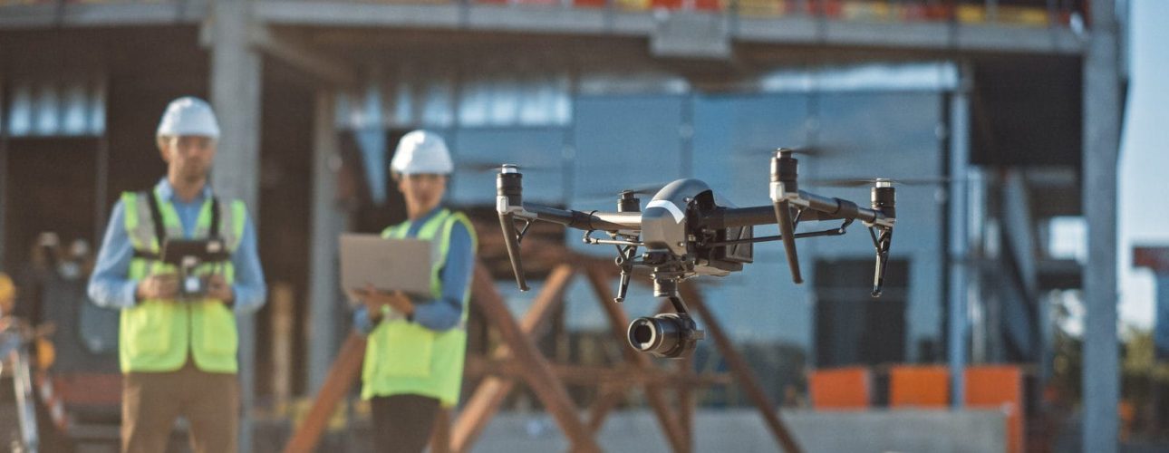 Diverse Team of Specialists Pilot Drone on Construction Site. Ar Two construction workers operate a survey drone on a work site.
